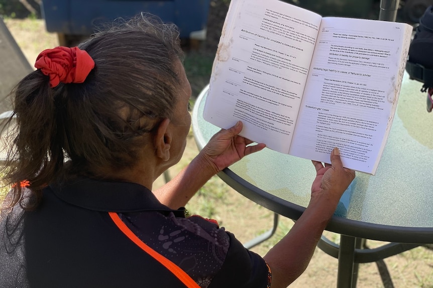 An Indigenous woman sitting with her back to the camera, hair in ponytail, reading a textbook.
