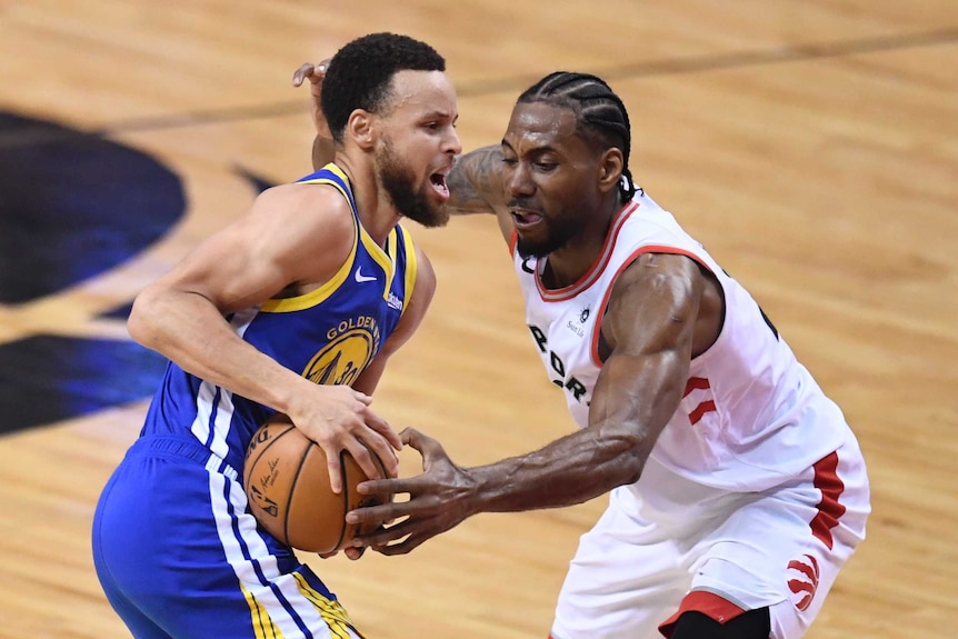 Stephen Curry holds the ball at hip level as Kawhi Leonard uses his left hand to try to steal the ball.