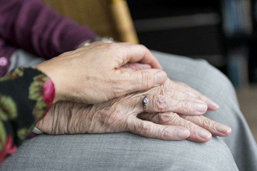 A close-up shot of a hand resting on an elderly woman's hands.