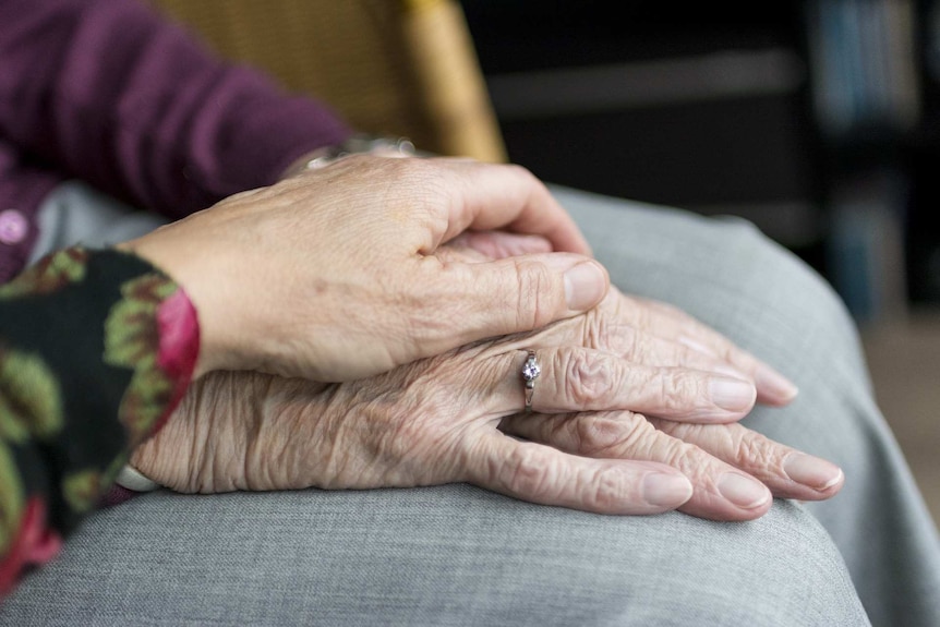 A close-up shot of a hand resting on an elderly woman's hands.