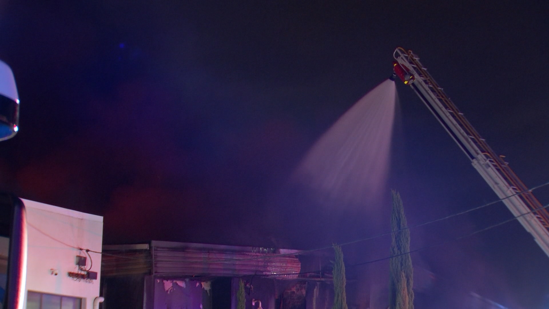 Water is sprayed onto a building from the top of a long white ladder that reaches into the sky at night.