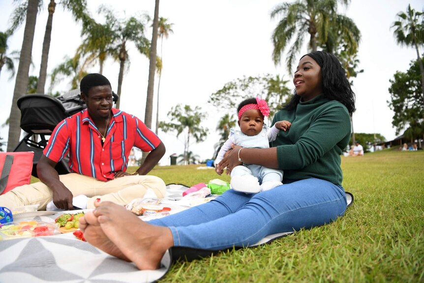 A mother, husband and their baby on a picnic rug in the park