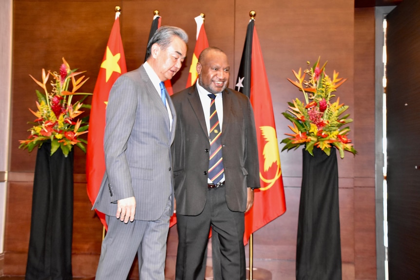 Wang Yi in a suit standing next to James Marape in front of Chinese and PNG flags.