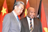 Wang Yi in a suit standing next to James Marape in front of Chinese and PNG flags.