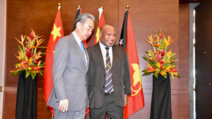 Wang Yi in a suit standing next to James Marape in front of Chinese and PNG flags.