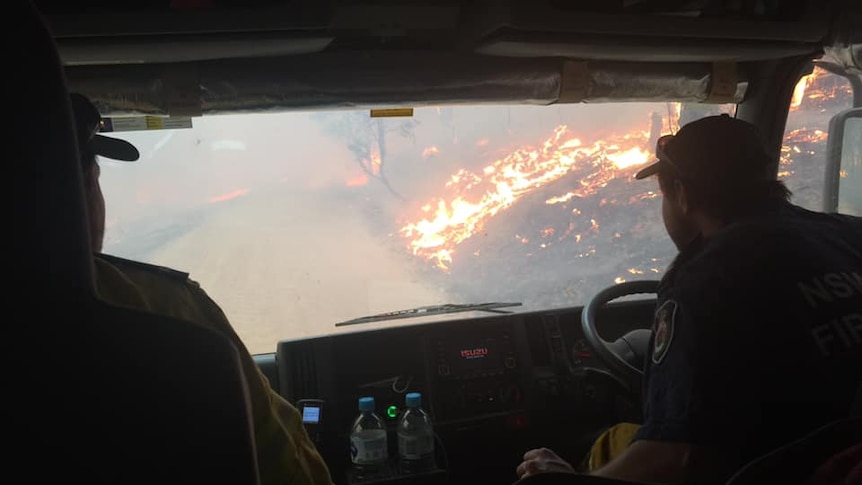 Two firefighters in a truck, looking out at bushfires.
