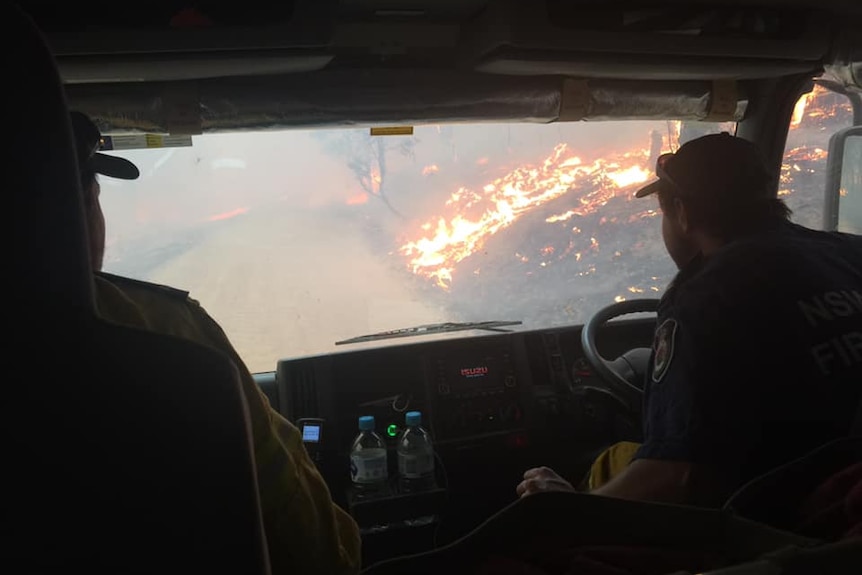 Two firefighters in a truck, looking out at bushfires.