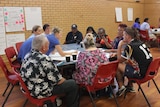 A group of indigenous and non-indigenous people gathered around a table writing on butcher's paper