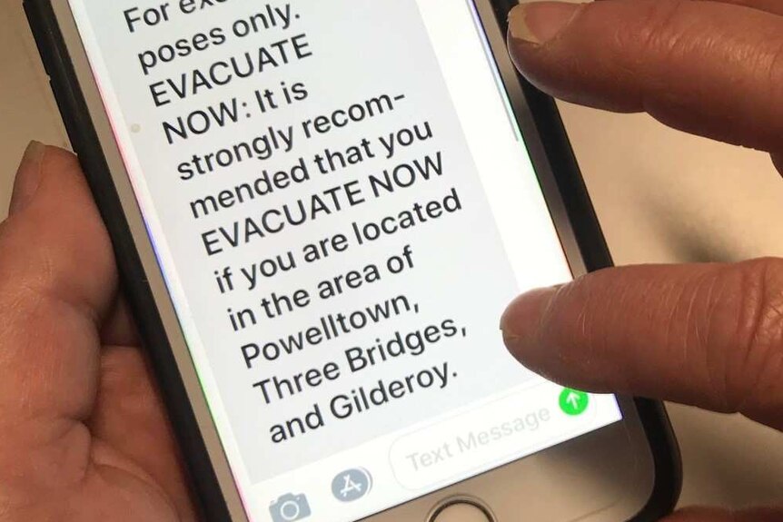 Hands holding a phone, which has a text message saying 'For exercise purposes only. EVACUATE NOW'.