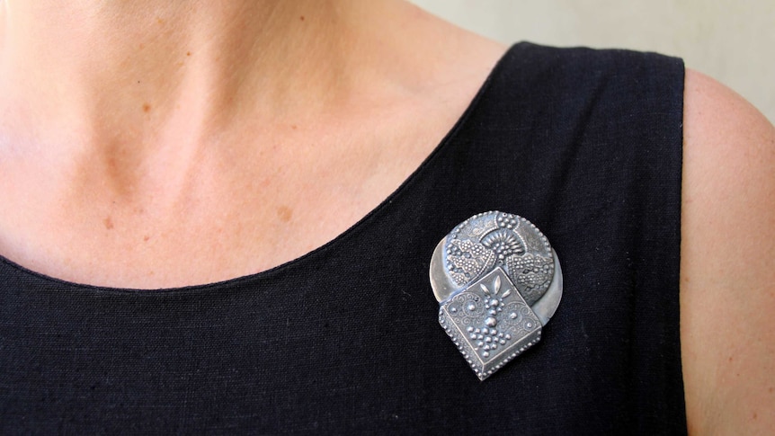 A close-up of a women's neck and an ornate broach.