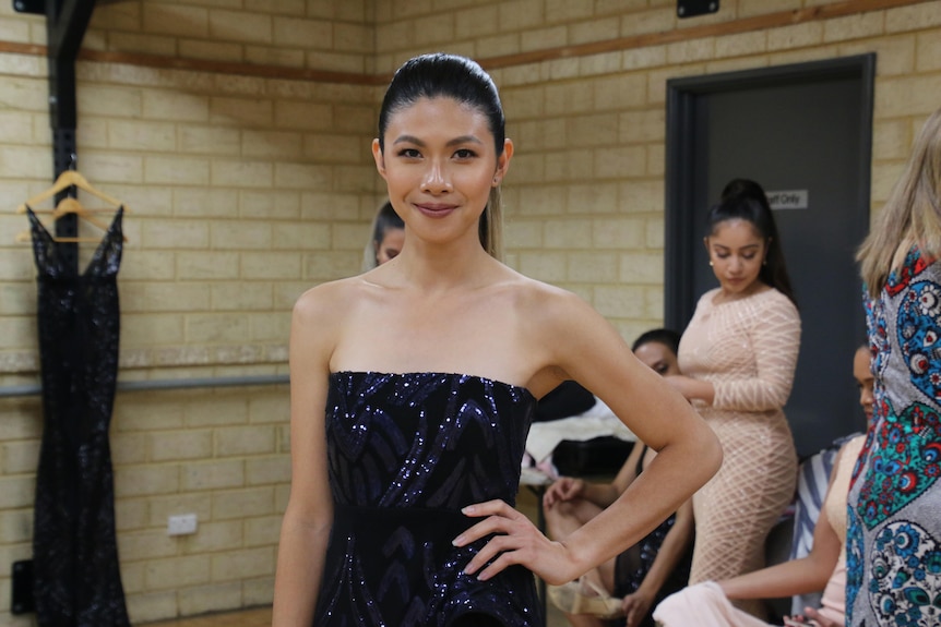 A young woman poses for a photo backstage at a fashion show wearing a black outfit.