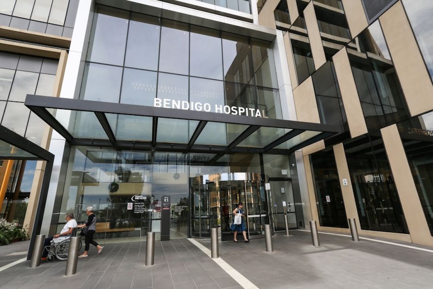 The entrance to a hospital with people walking in and out of it.