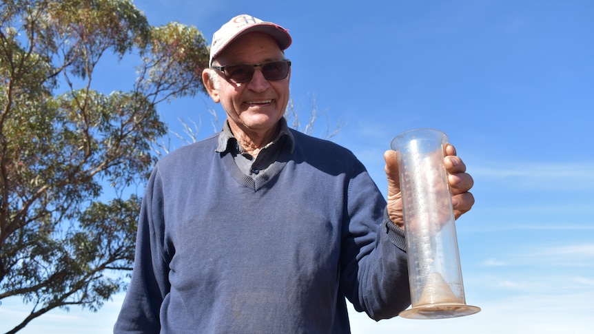 A smiling older man holding a rain gauge.