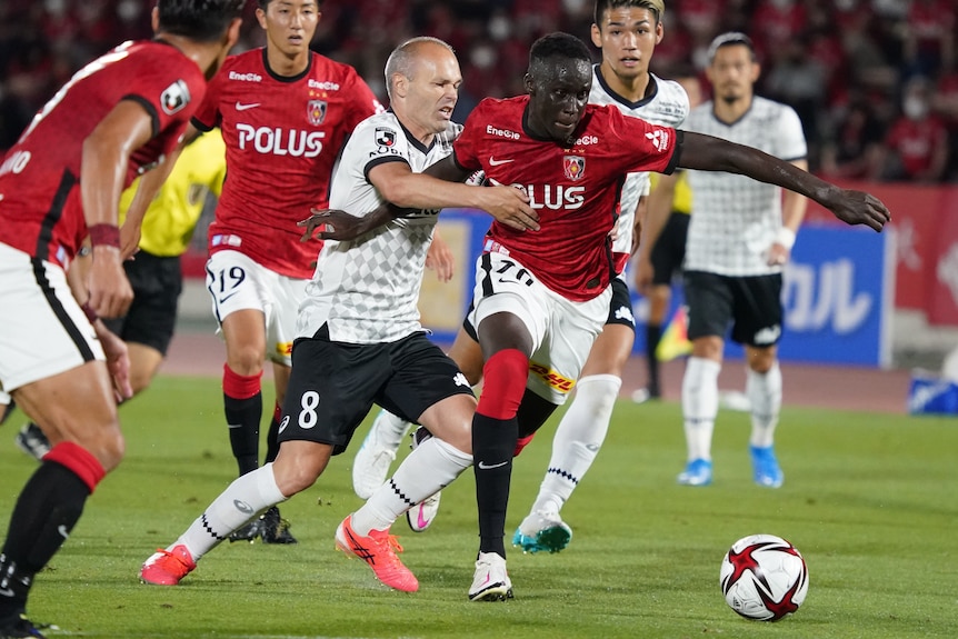 Two men's soccer teams, one wearing red and white and the other wearing black and white, battle for the ball