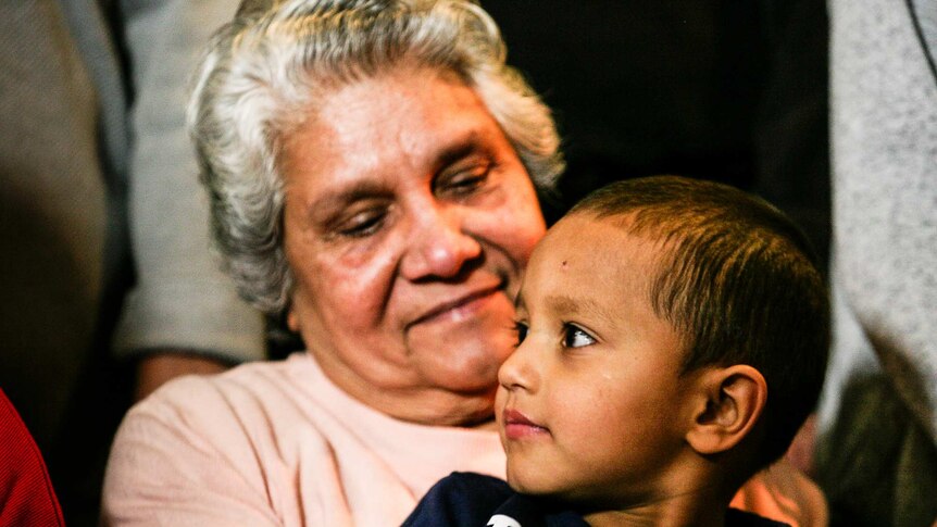 An elderly Indian woman smiles at her young grandson as she holds him in her lap