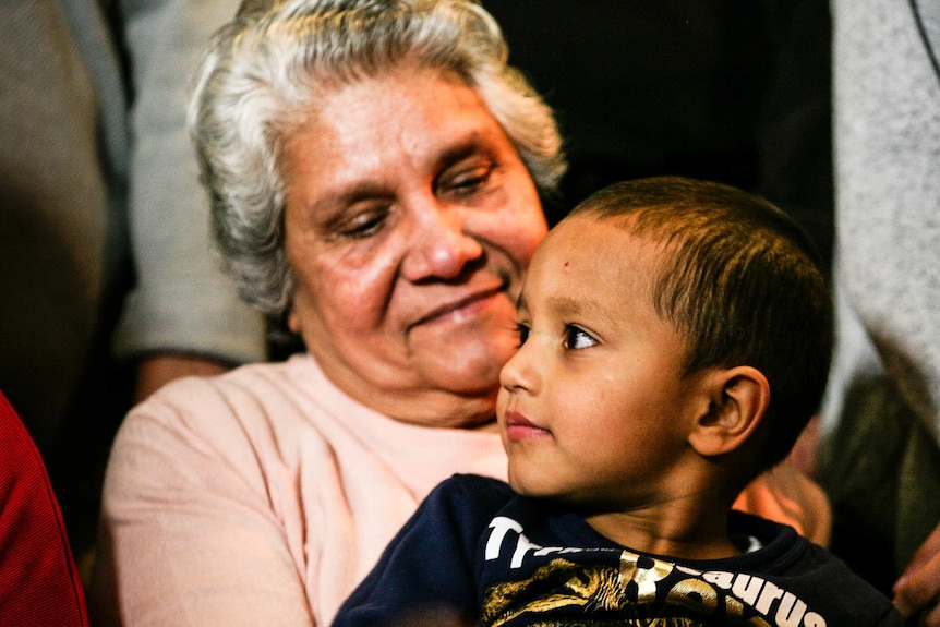 An elderly Indian woman smiles at her young grandson as she holds him in her lap