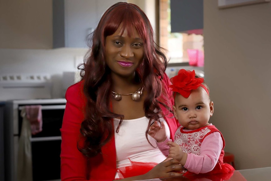 Lucy Kalwila sitting at her kitchen table with her daughter on her lap