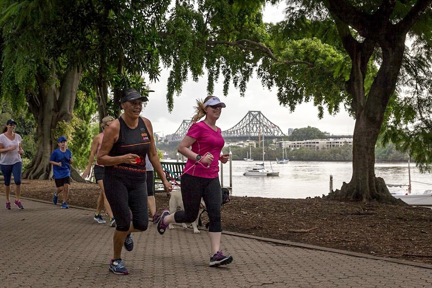 Two women running with a pink tether in a park in Brisbane