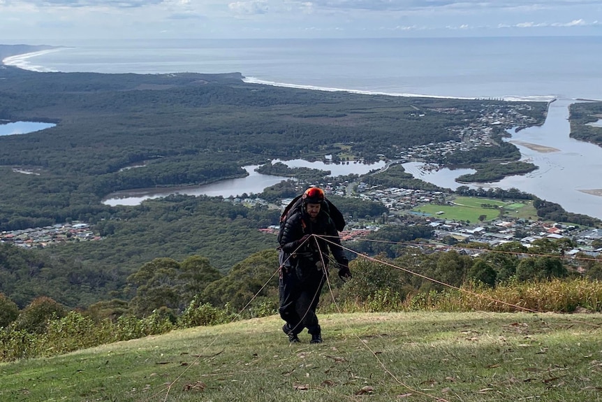 Man in paragliding suit prepares to jump off side of mountain 