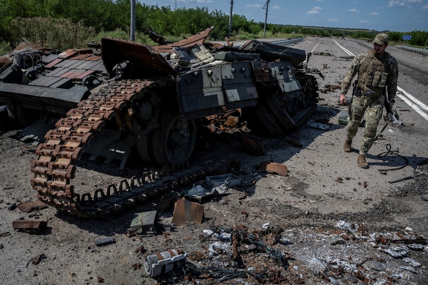 A man looking at a destroyed vehicle near a road.