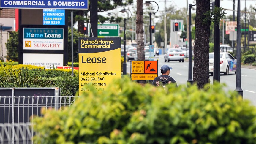 A man walks down Gympie Road at Strathpine past a Lease sign.