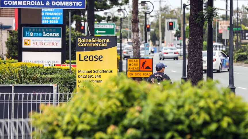 A man walks down Gympie Road at Strathpine past a Lease sign.