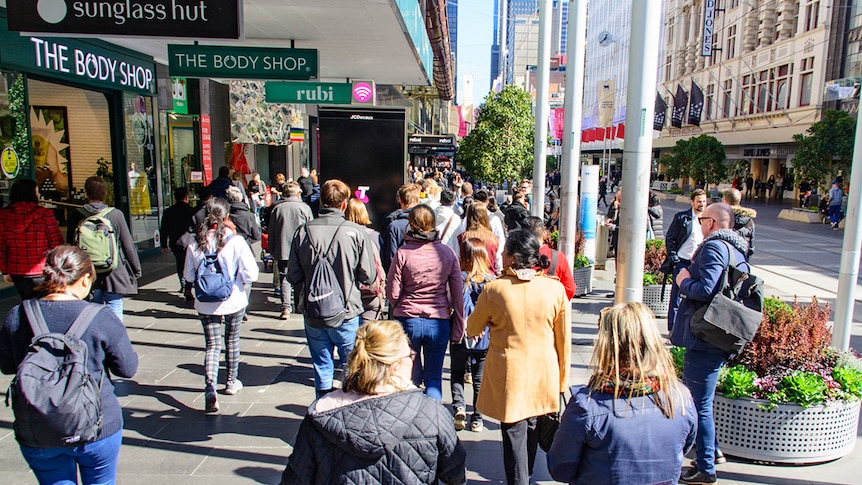 A large number of pedestrians walk down a busy shopping strip in the Melbourne CBD.