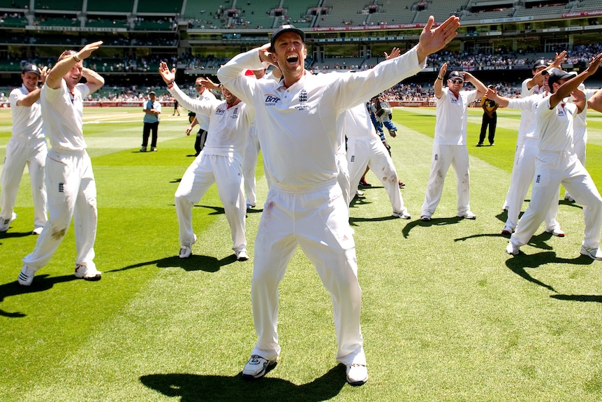 Graeme Swann stands with one arm stretched out in front of him and the other holding the back of his head, smiling