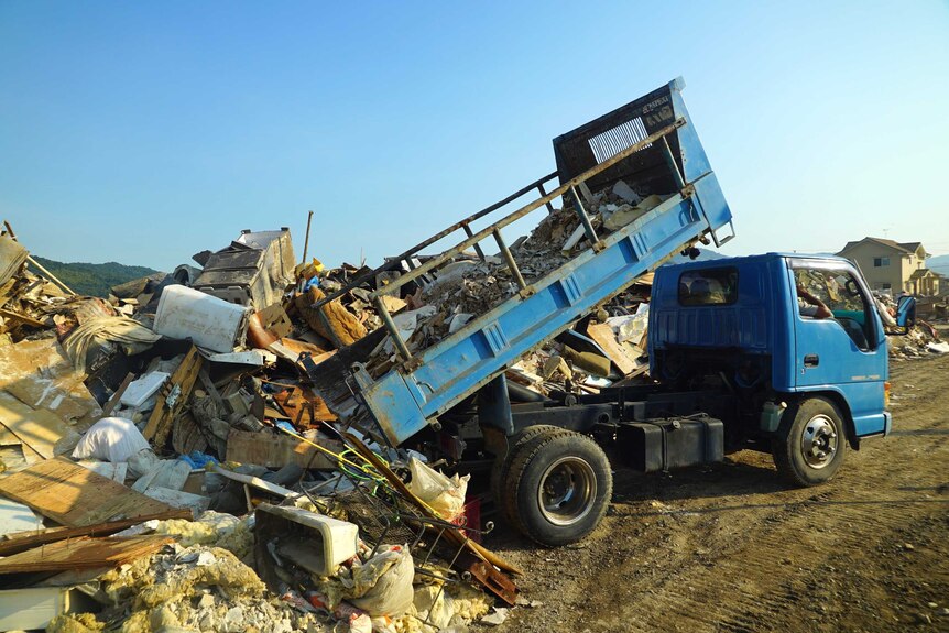 Rubbish is tipped out of the back of a truck onto a big pile.