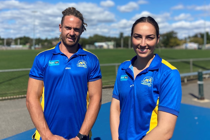 Two people standing in front of a football oval. 