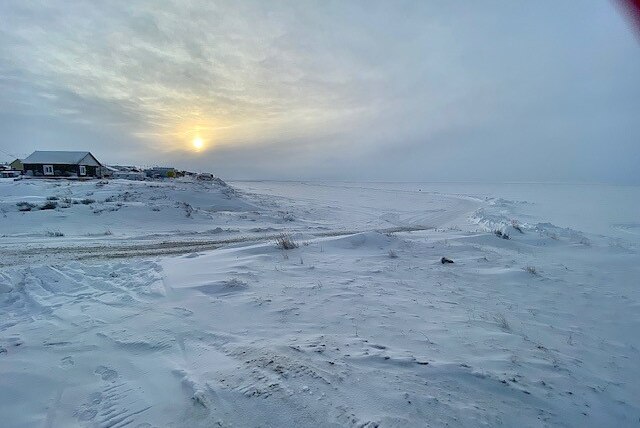 An open area covered in snow and ice, with a cloudy ski and sun setting in background.