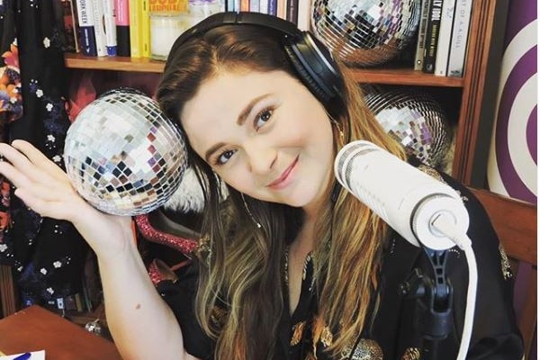 A woman in headphones next to a microphone holds a disco ball