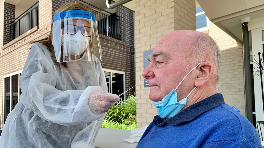 Mężczyzna badany pod kątem COVID-19 przez pielęgniarkę nosi osłonę twarzy.