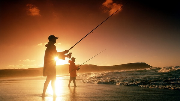 silhouette of two men fishing from shore with bright sun in background