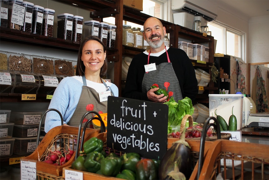 Chris Barker and Helen Piper stand inside the shop with fruit and vegetables in the foreground.