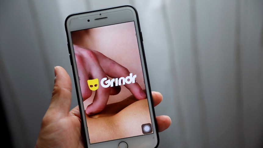 A person holding a phone and using dating app Grindr.