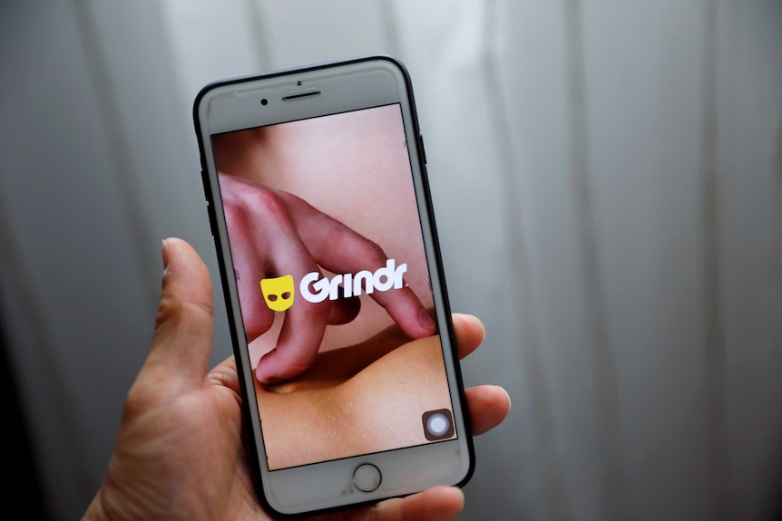 A person holding a phone and using dating app Grindr.