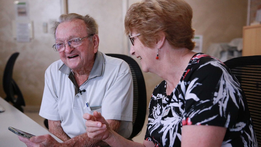 Desmond White and Sandra Keen sit leaning over an iPhone and laughing.