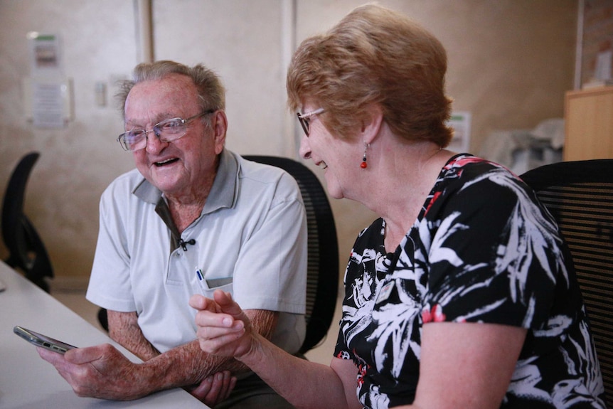 Desmond White and Sandra Keen sit leaning over an iPhone and laughing.