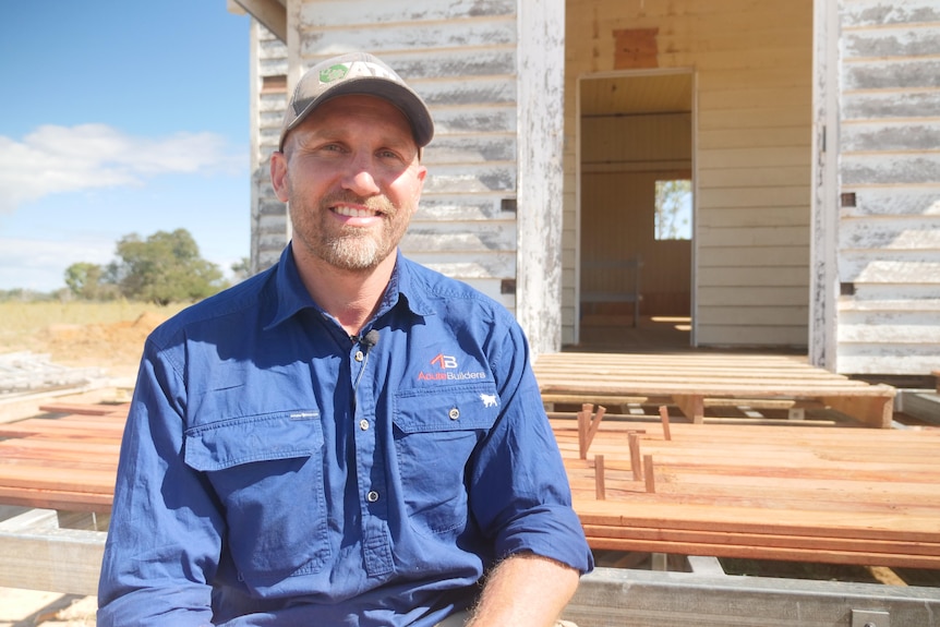 A man in a blue uniform and cap sitting on steps in front of an old, tiny church.