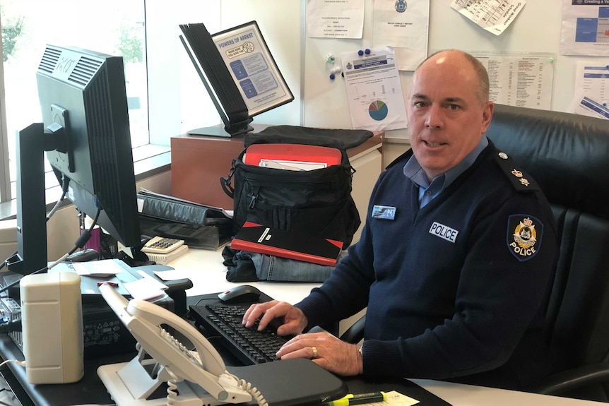 Superintendent Mike Bell sitting at a desk in front of a computer wearing police uniform