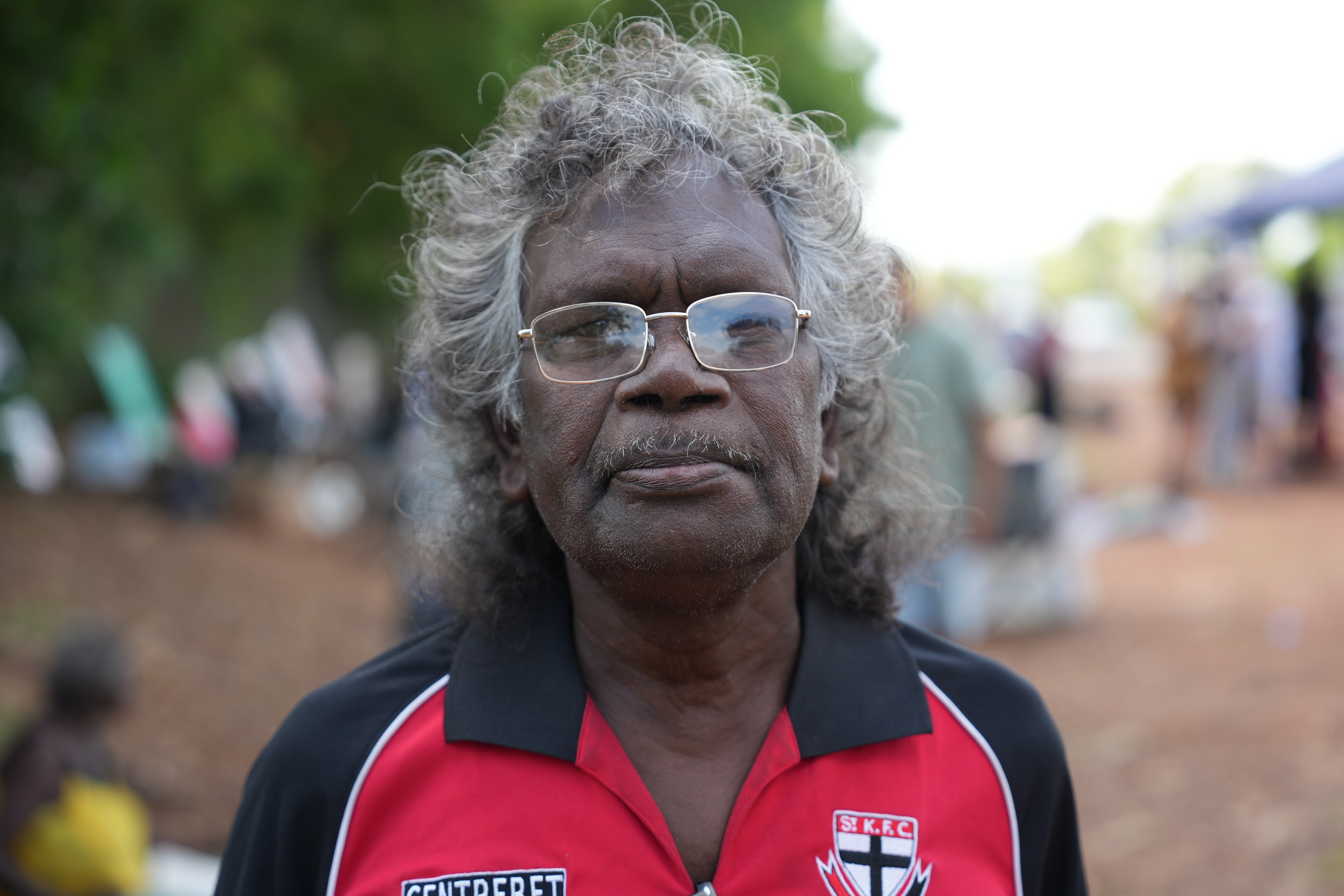 A close-up portrait of Harry Garruwurra who wears spectacles and a St Kilda Football Club polo shirt.