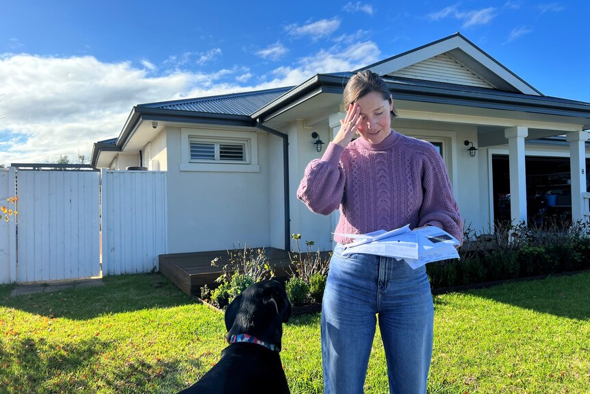 A woman standing out the front of a house with bills in hand 