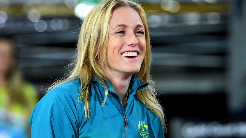 A young blonde white woman wearing a tracksuit top with an Australian emblem smiles