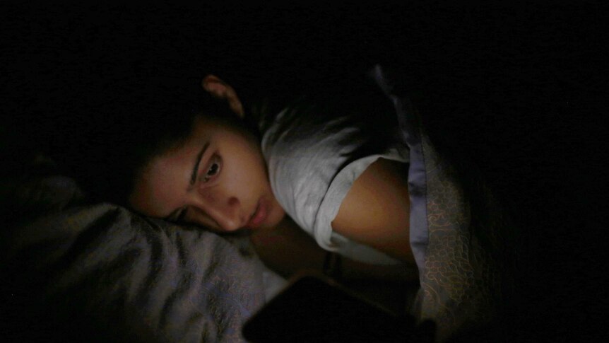 Somya looks at her phone as she lies in bed.