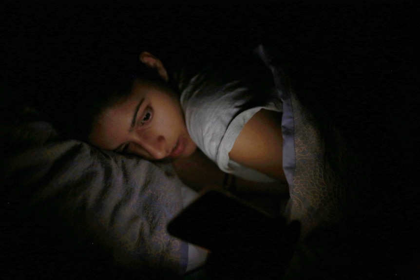 Somya looks at her phone as she lies in bed.
