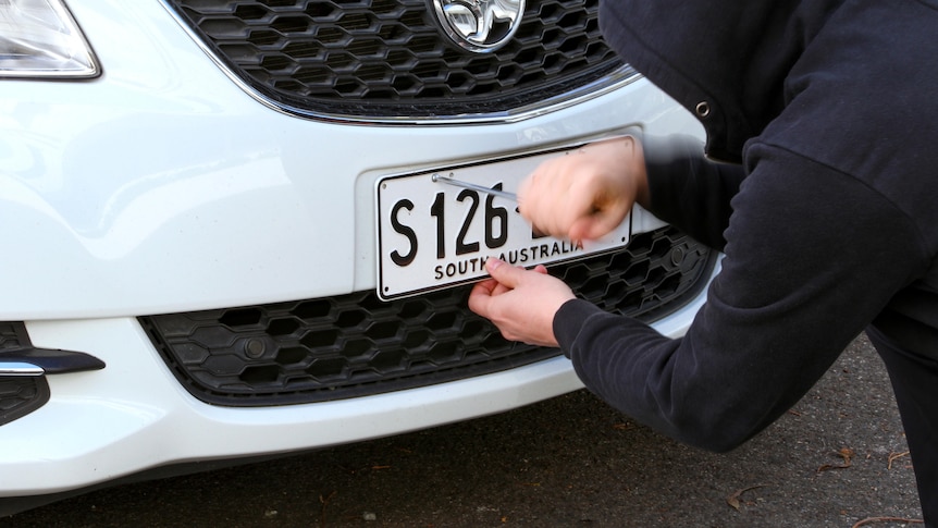 A person in a hooded top removes a number plate.