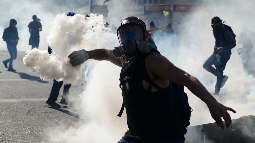 Protester in a mask hurls a canister back at police, shrouded dramatically in smoke
