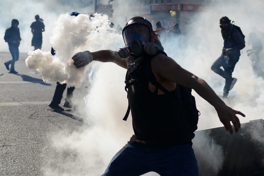 Protester in a mask hurls a canister back at police, shrouded dramatically in smoke