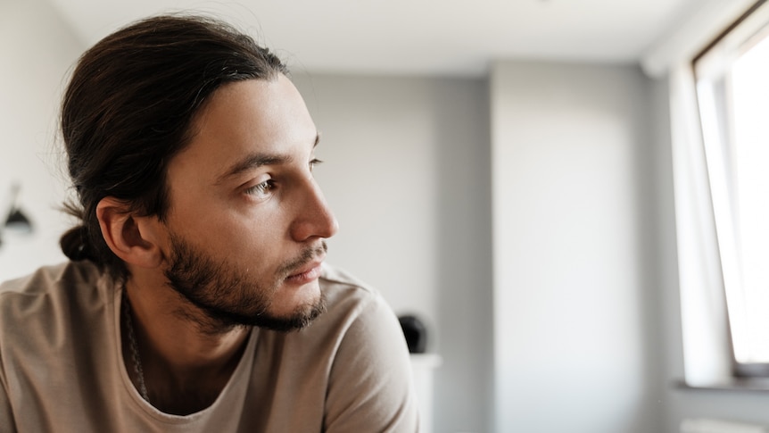 A man looks out of the window, in story about coping with anxiety about lockdown lifting and restrictions easing.